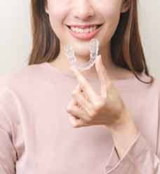 Closeup of someone holding an Invisalign tray above its container with a light blue background