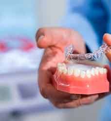 Nose-to-chest view of a woman in a beige shirt holding Invisalign to close to her smile