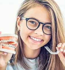 Young woman with purple nails and brown hair outside smiling holding Invisalign