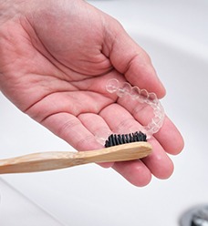 Patient using soft-bristled toothbrush to clean aligner