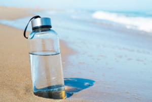 Clear, almost full water bottle stuck in beach sand